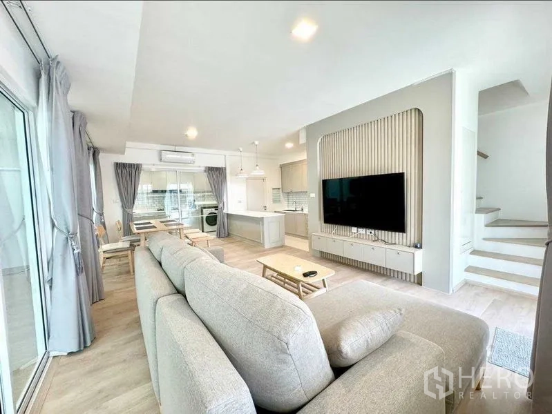 联排别墅 出租或出售在Prawet, Bangkok - 舒适客厅，转角沙发对面大屏电视，连接厨房与楼梯。