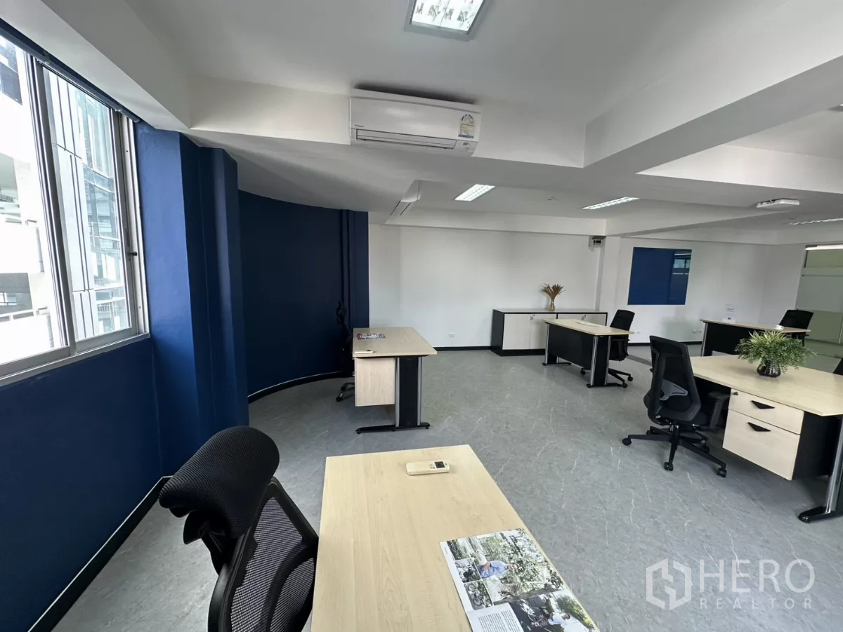 Office Space for rent in Watthana, Bangkok - Corner view by large windows with a curved blue feature wall and a single workstation.