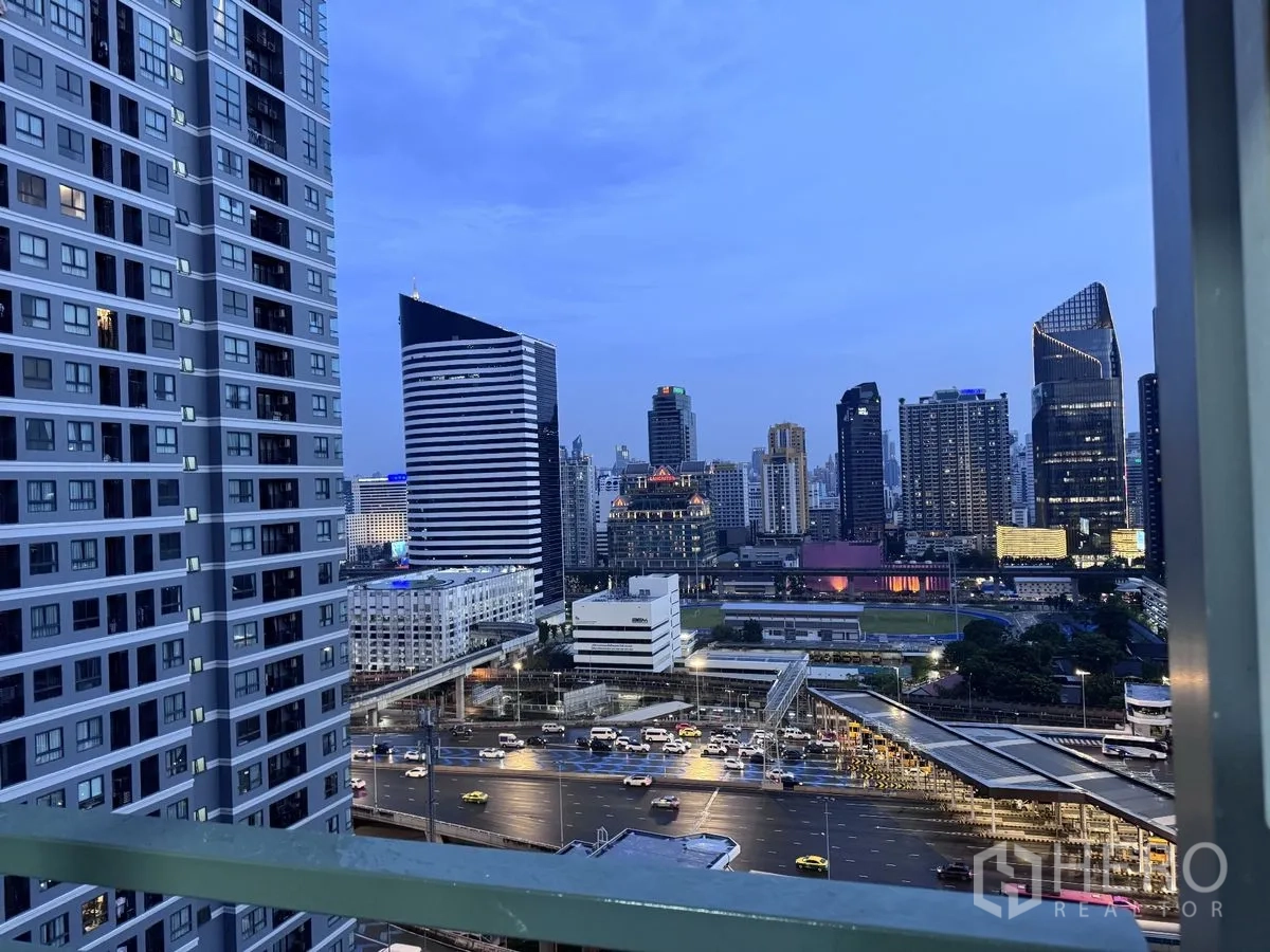 Condominium for rent in Huai Khwang, Bangkok - High-floor balcony view of the city skyline at dusk with modern towers and busy roads.