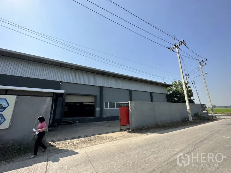 工厂 出租在Lam Luk Ka, Pathum Thani - 临街灰色工厂外观，带卷帘装卸门、红色大门与围墙。