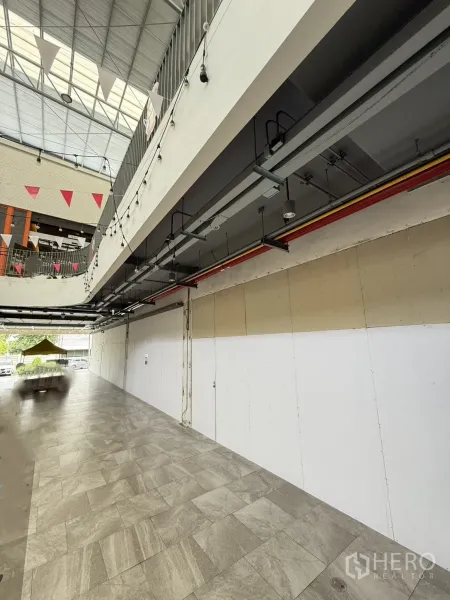 零售空间 出租 - 一层商铺外沿步道，挑高顶棚与瓷砖地面，裸露灯带。