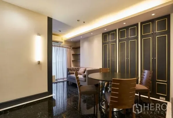 Condominium for sale in Ratchathewi, Bangkok - Open-plan living and dining with round table, built-in cabinets, sofa and black marble floor.