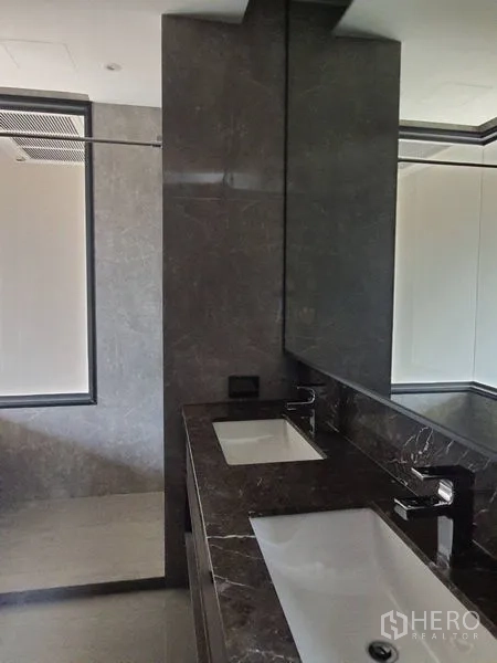Condominium for sale in Huai Khwang, Bangkok - Bathroom with double sinks, dark stone vanity and a large mirror.