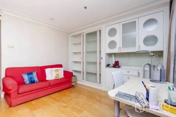 Condominium for rent or sale in Pathum Wan, Bangkok - Multipurpose room with red sofa, built-in shelves, and white work desk on wood flooring.