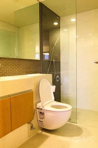 Condominium for rent in Watthana, Bangkok - Modern bathroom with glass-enclosed shower, wall-hung toilet and stone vanity.