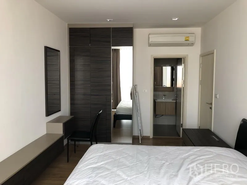 Condominium for rent in Watthana, Bangkok - Master bedroom with built-in wardrobe, dressing area, and doorway to an en-suite bathroom.