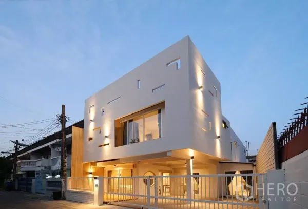 Townhouse for rent or sale in Watthana, Bangkok - Modern cubic white townhouse facade at dusk with warm lighting and gated carport in Sukhumvit 71.