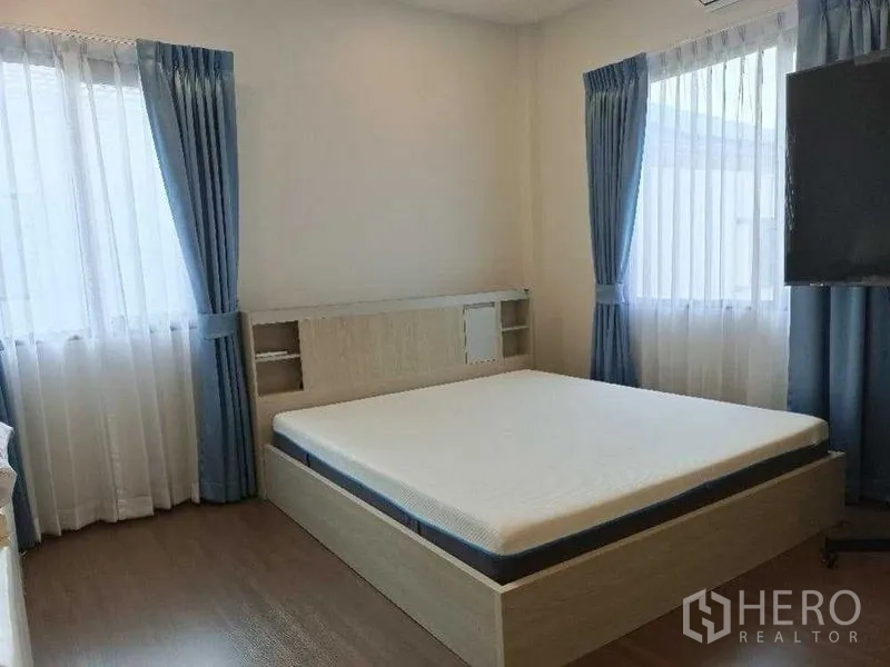 บ้าน ให้เช่าในMueang Nonthaburi, Nonthaburi - ห้องนอนสว่างด้วยหน้าต่างบานใหญ่ ผ้าม่านสีน้ำเงิน และเตียงควีนบนพื้นไม้