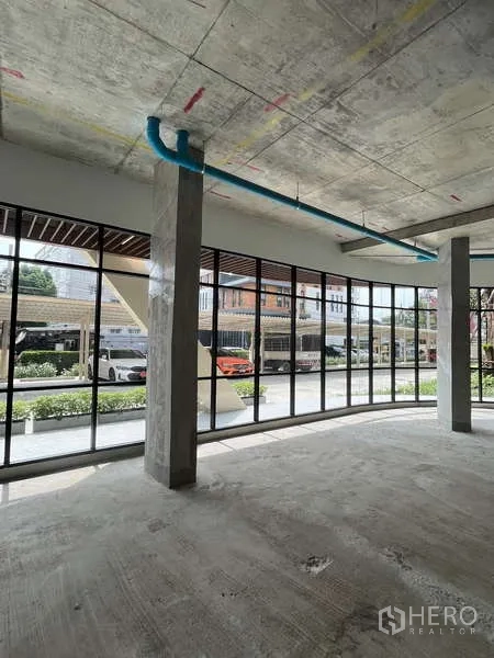 零售空间 出租在Phra Khanong, Bangkok - 开放式营业空间，混凝土柱、蓝色管线与外部停车位