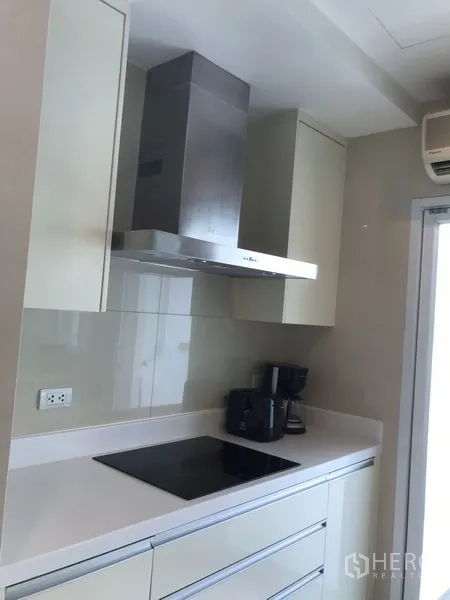 房间 出租在Khlong Toei, Bangkok - 现代封闭式厨房，电磁炉、抽油烟机与简洁橱柜。