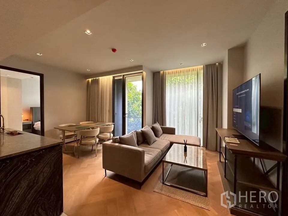 Condominium for rent in Watthana, Bangkok - Cozy lounge with TV, sofa and sheer curtains opening to green outlook.