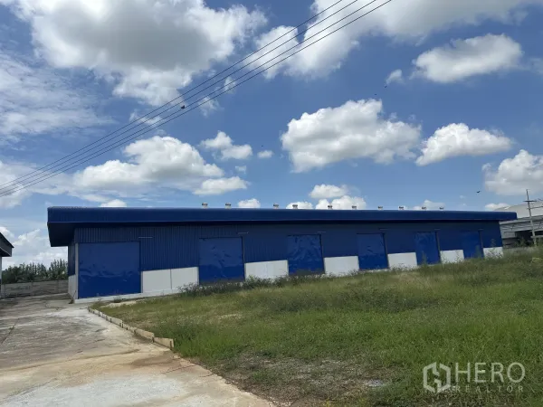Warehouse for rent in Bang Len, Nakhon Pathom - Long facade of warehouse with roof ventilators and several loading bays next to grass verge.