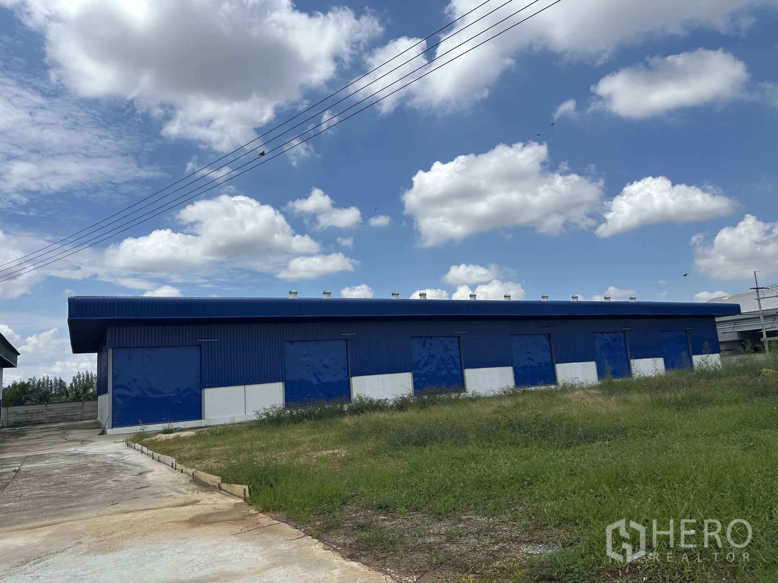 Warehouse for rent in Bang Len, Nakhon Pathom - Long facade of warehouse with roof ventilators and several loading bays next to grass verge.