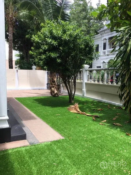 Detached House for rent in Khlong Toei, Bangkok - Side garden with lush green lawn, mature trees and a white boundary fence.