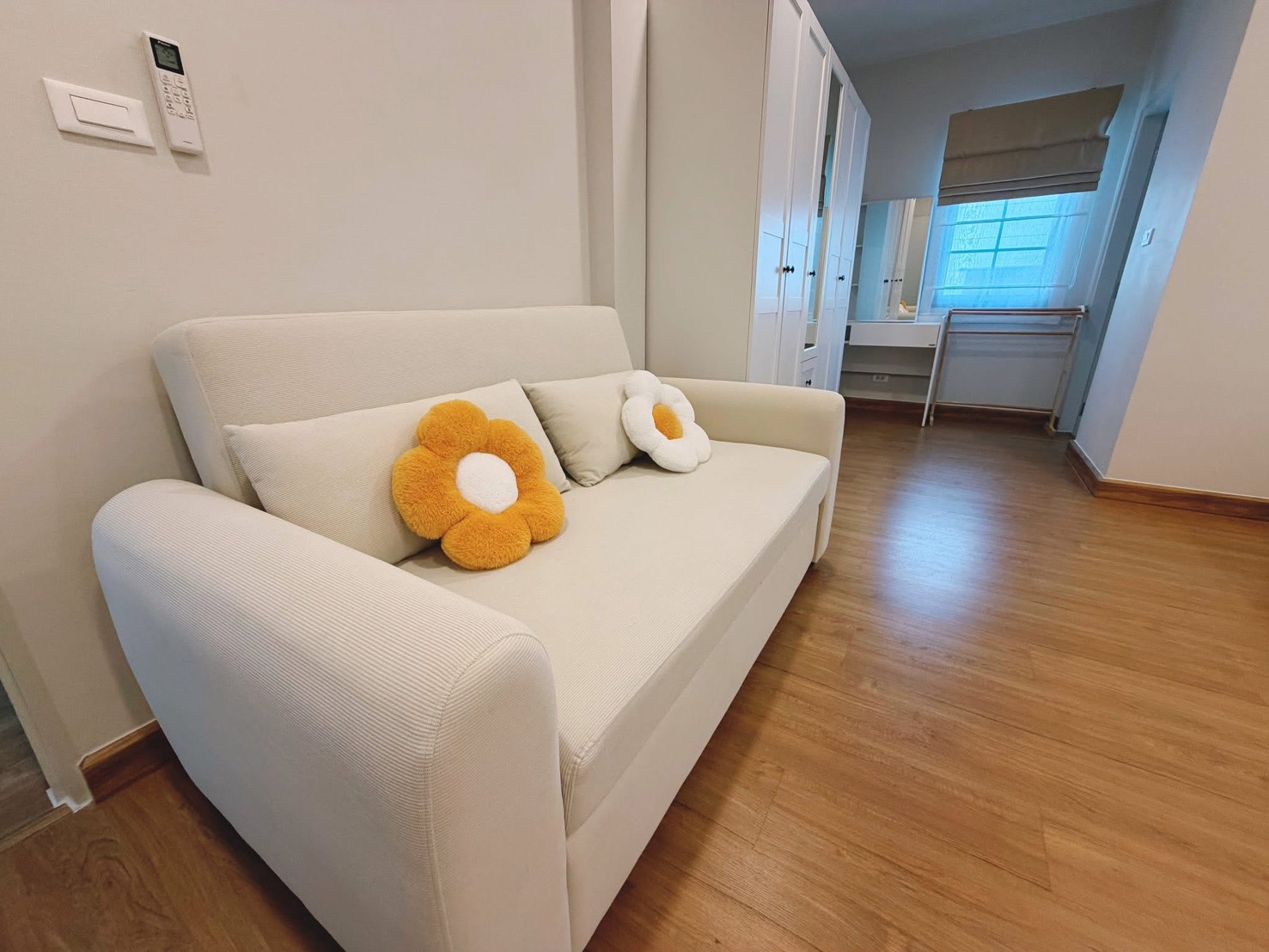 独立式住宅 出租在Bang Phli, Samut Prakan - 温馨小客区，米色双人沙发与抱枕，旁有衣柜与窗户。