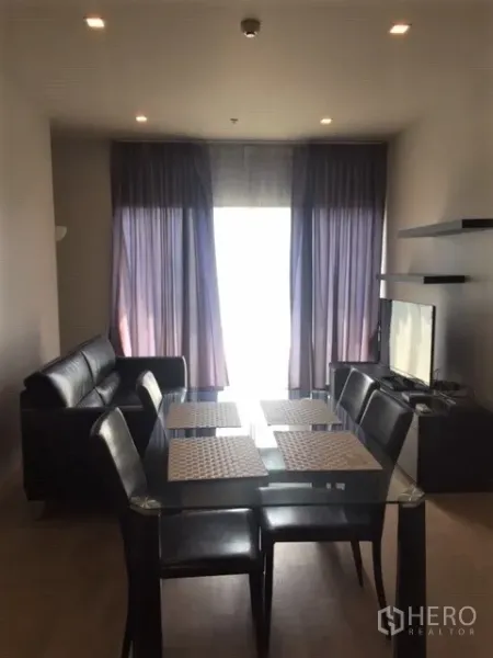 คอนโด ให้เช่าในBangkok - พื้นที่นั่งเล่นและทานอาหารแบบโอเพนแพลน โต๊ะกระจก โซฟาหนัง ทีวี และผ้าม่านสูงจรดเพดาน ในคอนโด 2 ห้องนอนใกล้ BTS พร้อมพงษ์