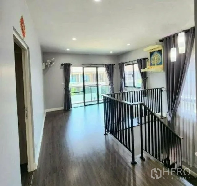 Detached House for sale in Pathum Thani - Sunlit upstairs family area with balcony access and a black metal staircase.