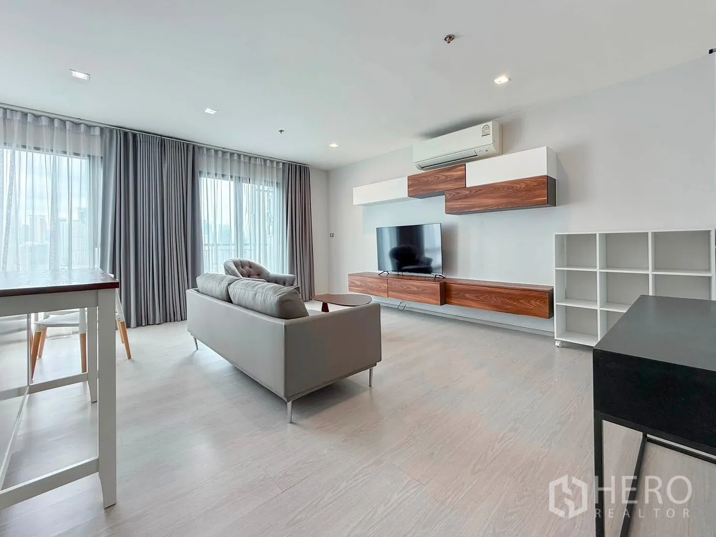 Condominium for rent in Khlong Toei, Bangkok - Open living room with sofa, TV wall unit, and floor-to-ceiling windows.