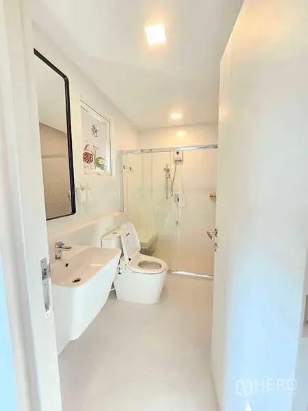 Detached House for rent or sale in Prawet, Bangkok - Modern white bathroom with glass-enclosed shower, vanity and toilet.
