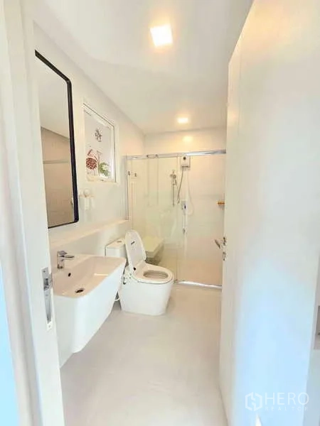 Detached House for rent or sale in Prawet, Bangkok - Modern white bathroom with glass-enclosed shower, vanity and toilet.