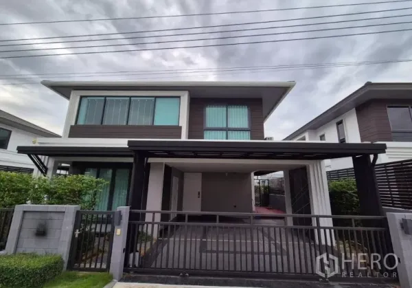 独立式住宅 出售在Bang Kruai, Nonthaburi - 两层独栋别墅外观，带前院大门与车棚，绿篱环绕，位于暖武里府Bang Kruai。