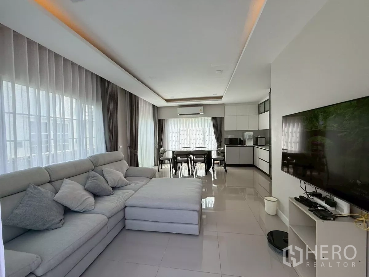 Detached House for rent in Bang Phli, Samut Prakan - Bright open-plan living area with large sectional sofa, TV wall and dining table by windows.