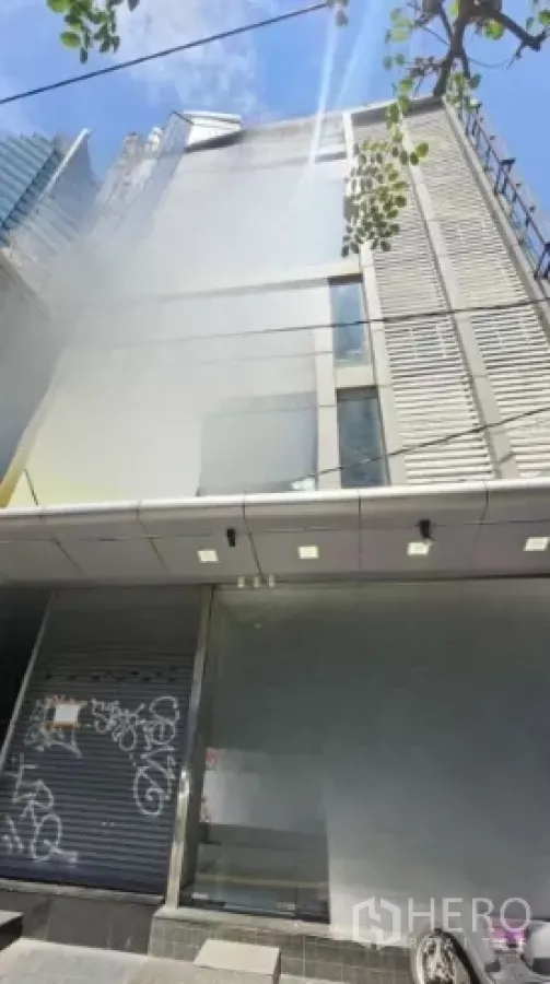 零售空间 出租在Watthana, Bangkok - 曼谷一栋中高层商业楼外观，金属立面与卷帘门，晴天街景。