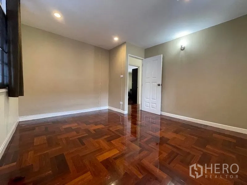 Detached House for rent in Khlong Toei, Bangkok - Empty bedroom with glossy parquet flooring, recessed lighting and window.