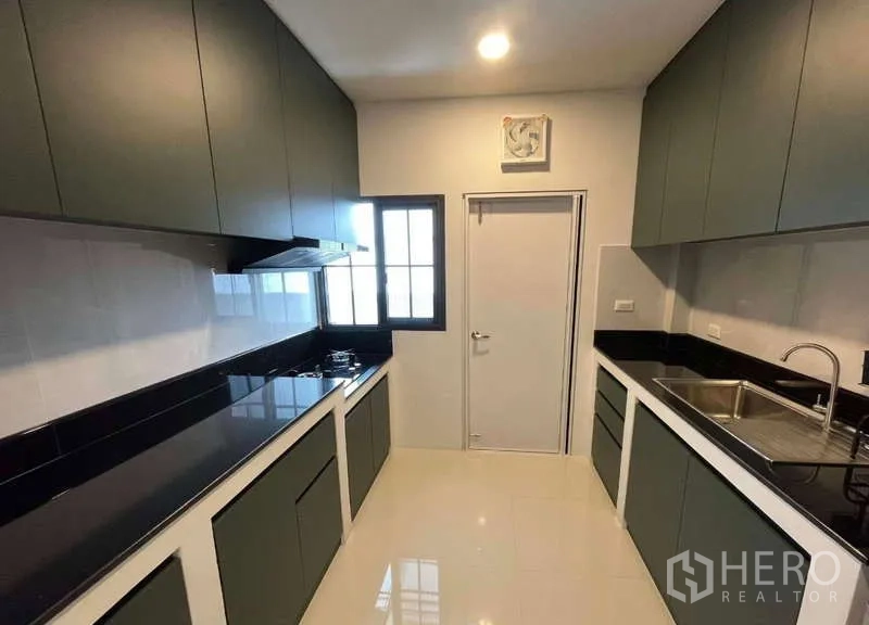 Detached House for rent in Bang Phli, Samut Prakan - Modern galley kitchen with black countertops, gas hob, sink and ample cabinetry