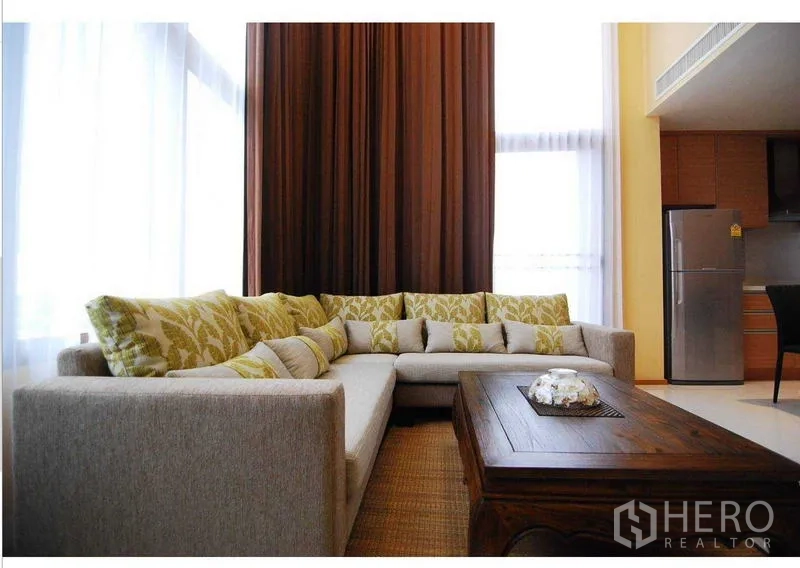 คอนโด ให้เช่า - โซฟาตัวแอลพร้อมหมอนลาย ใต้ผ้าม่านสูงและโต๊ะกาแฟไม้ เพดานสูงโปร่ง