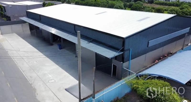 Warehouse for rent in Bang Bua Thong, Nonthaburi - Front facade of the warehouse with large canopy, drive-in loading bays, and a secure perimeter wall.