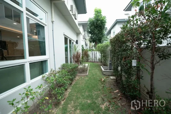 Detached House for rent or sale in Prawet, Bangkok - Narrow garden walkway with hedges and sliding windows along the house.