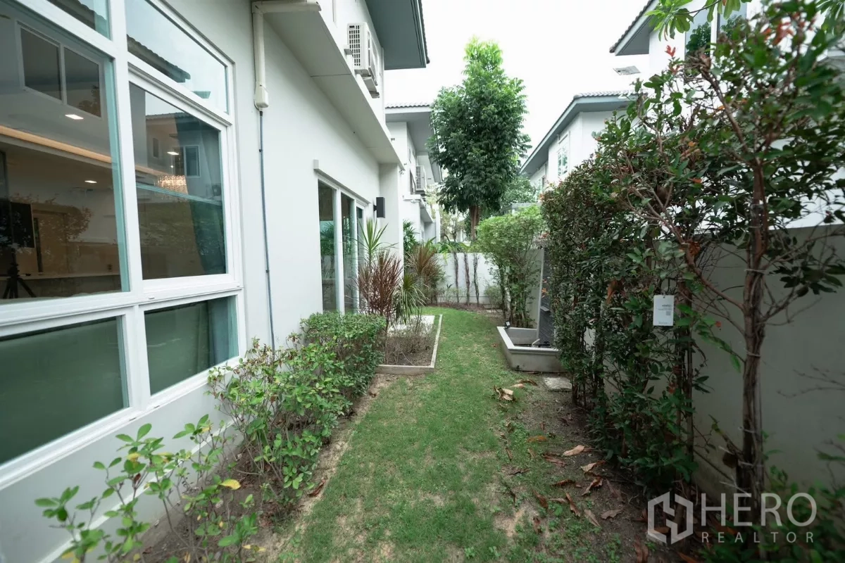 Detached House for rent or sale in Prawet, Bangkok - Narrow garden walkway with hedges and sliding windows along the house.