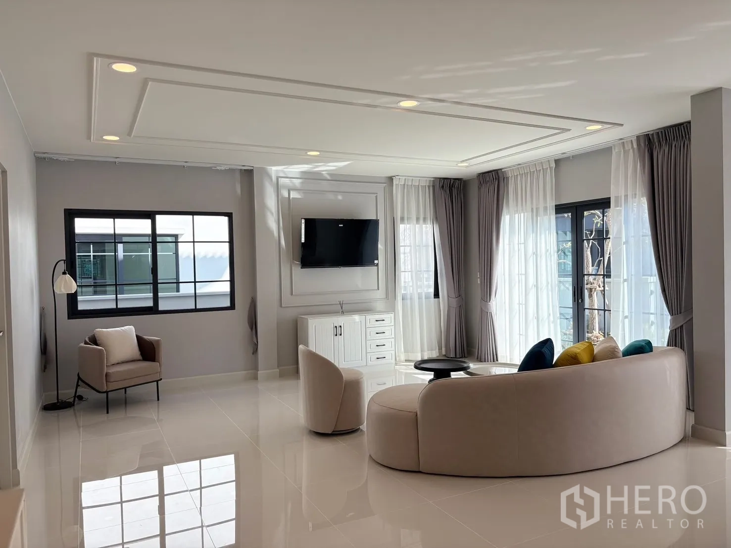 Detached House for rent in Bang Phli, Samut Prakan - Spacious living room with curved sofa, TV wall, floor-to-ceiling windows and glossy tile floors.