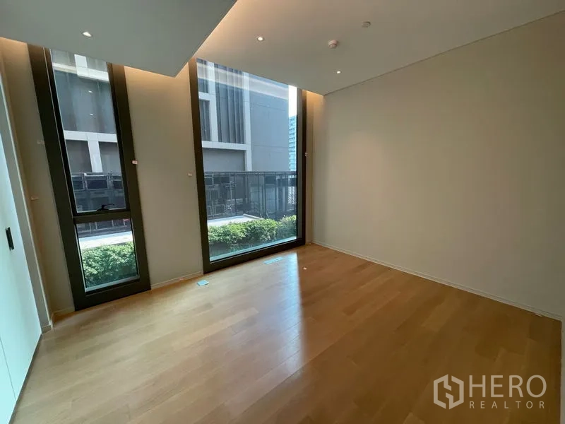 Condominium for rent or sale in Pathum Wan, Bangkok - Corner bedroom with tall windows and a quiet garden-level outlook.