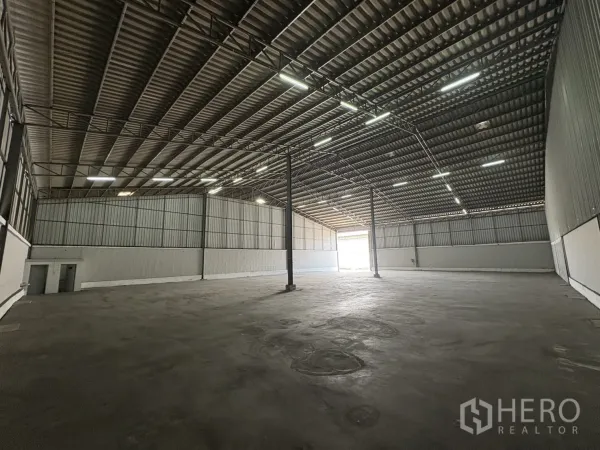 Warehouse for rent in Samut Prakan - Expansive storage area facing the entrance with smooth concrete floor and lined walls.