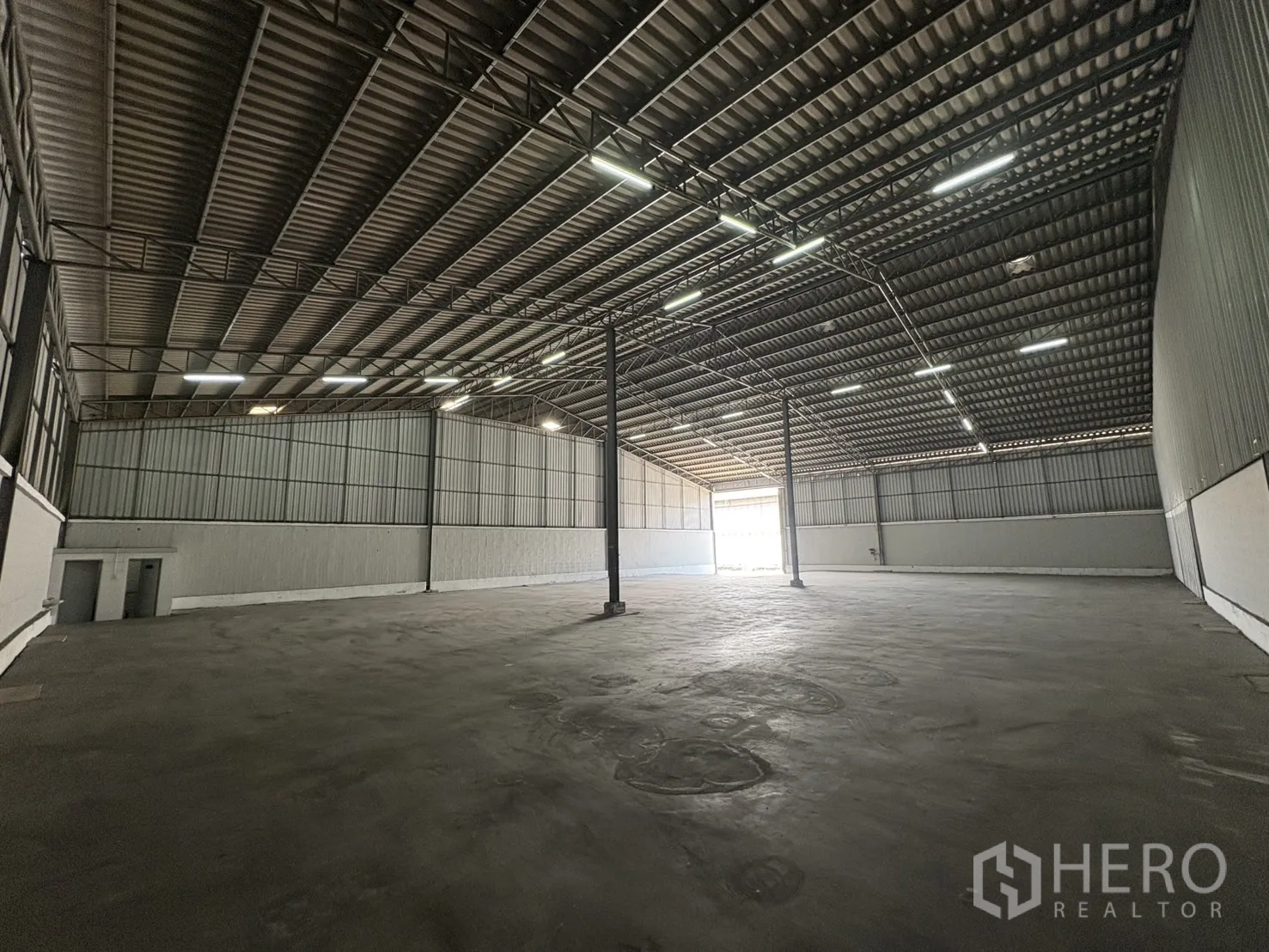 Warehouse for rent in Samut Prakan - Expansive storage area facing the entrance with smooth concrete floor and lined walls.
