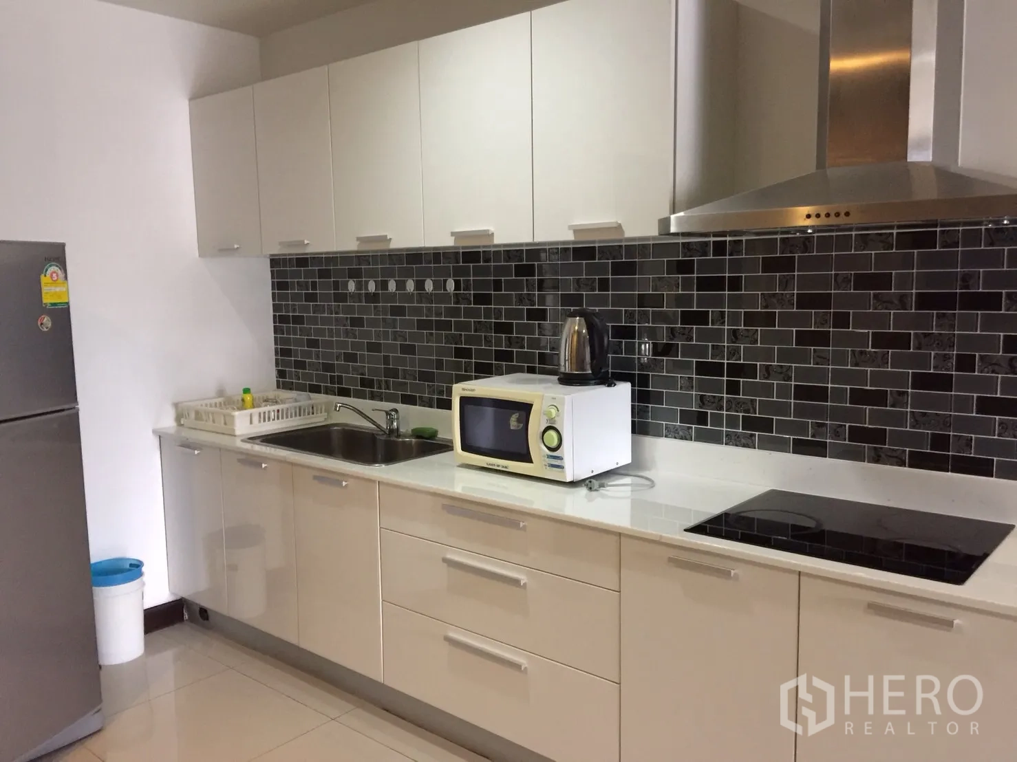 Condominium for rent in Watthana, Bangkok - Modern kitchen with white cabinetry, black subway-tile backsplash, hood, cooktop, microwave and refrigerator.