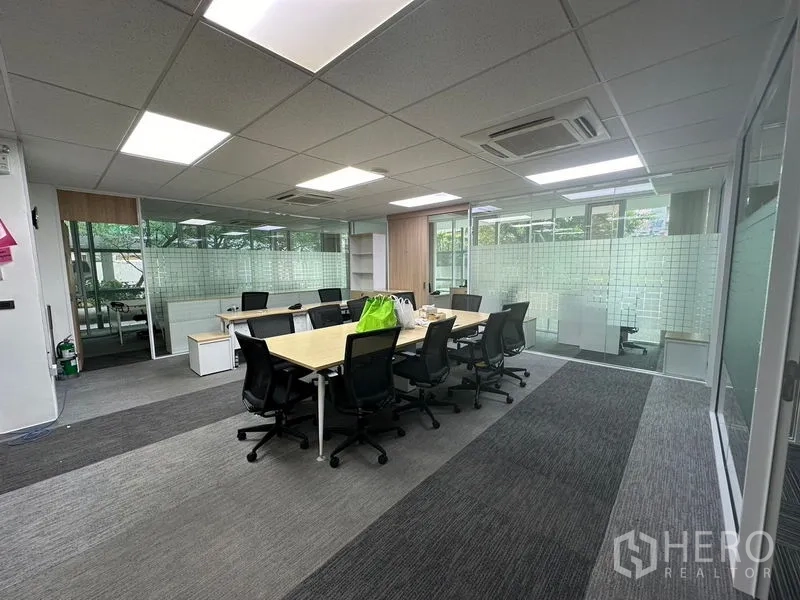 Office Space for rent - Open-plan office with long meeting table, ergonomic chairs, glass partitions, carpet tiles, and LED ceiling lights.