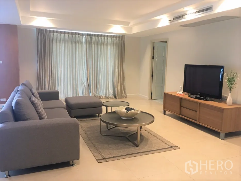 Condominium for rent in Watthana, Bangkok - Bright lounge featuring a TV console, full-length curtains, grey sofa, and round coffee tables on a rug.