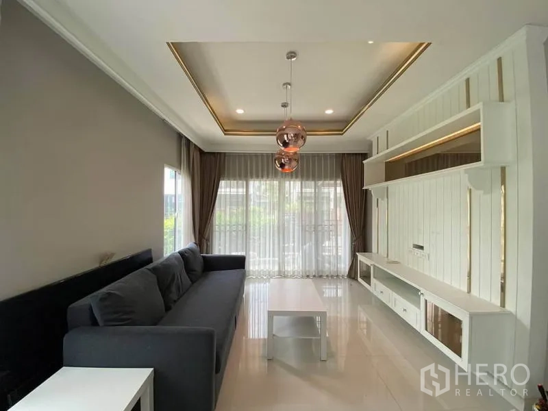 บ้าน ให้เช่าในSuan Luang, Bangkok - ห้องนั่งเล่นทันสมัย ม่านโปร่งจรดพื้น พร้อมผนังทีวีบิลต์อินและโคมเพดานดีไซน์