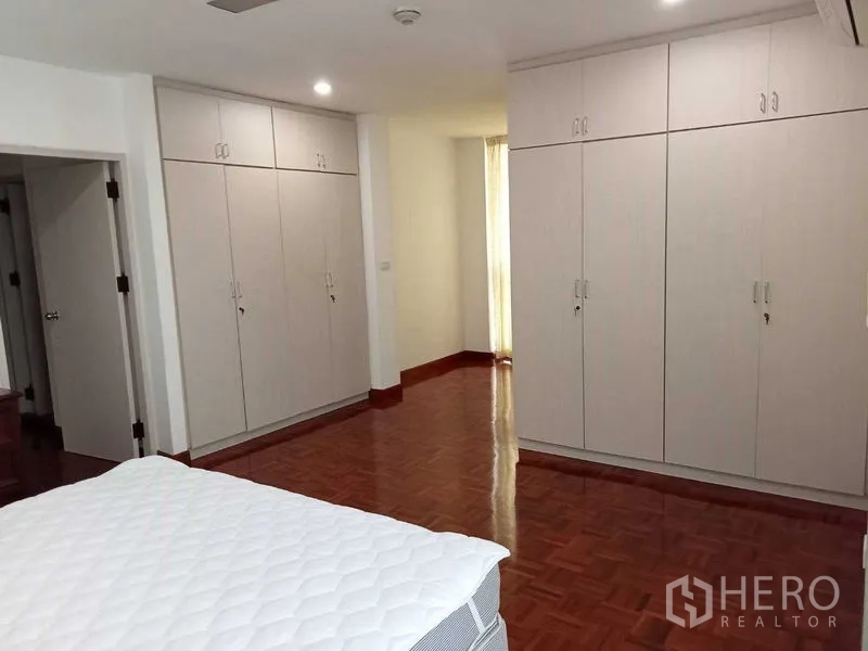Condominium for rent in Watthana, Bangkok - Master bedroom with multiple built-in wardrobes and polished wood flooring.