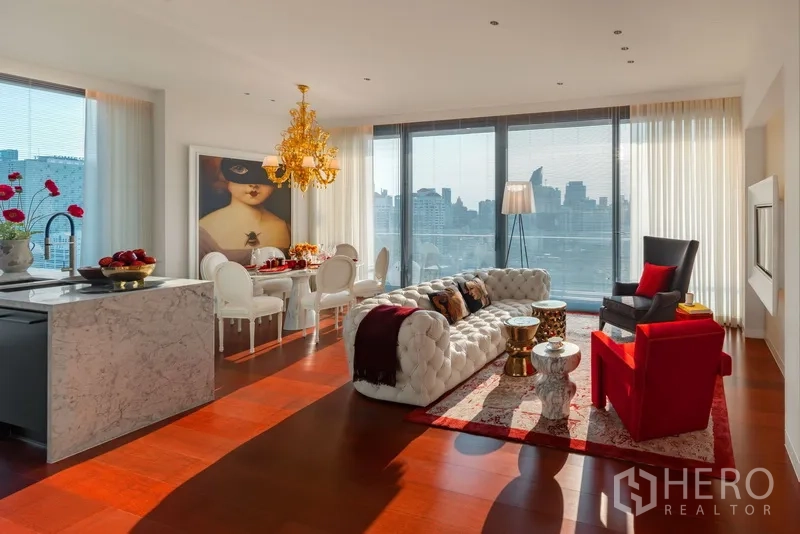 Condominium for sale in Watthana, Bangkok - Open‑plan living and dining room with chandelier, marble island kitchen and floor‑to‑ceiling windows facing the Bangkok skyline.