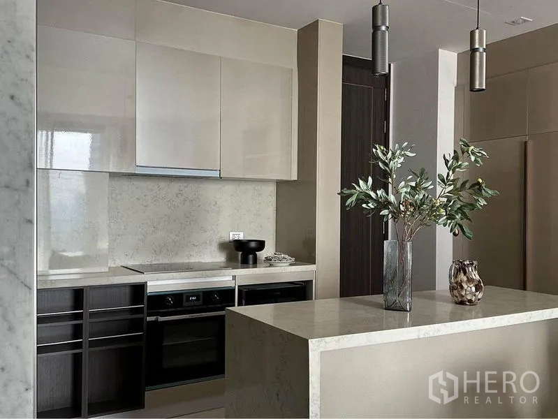Condominium for rent or sale in Watthana, Bangkok - Sleek kitchen featuring stone island, glossy cabinets, built-in ovens and pendant lights.