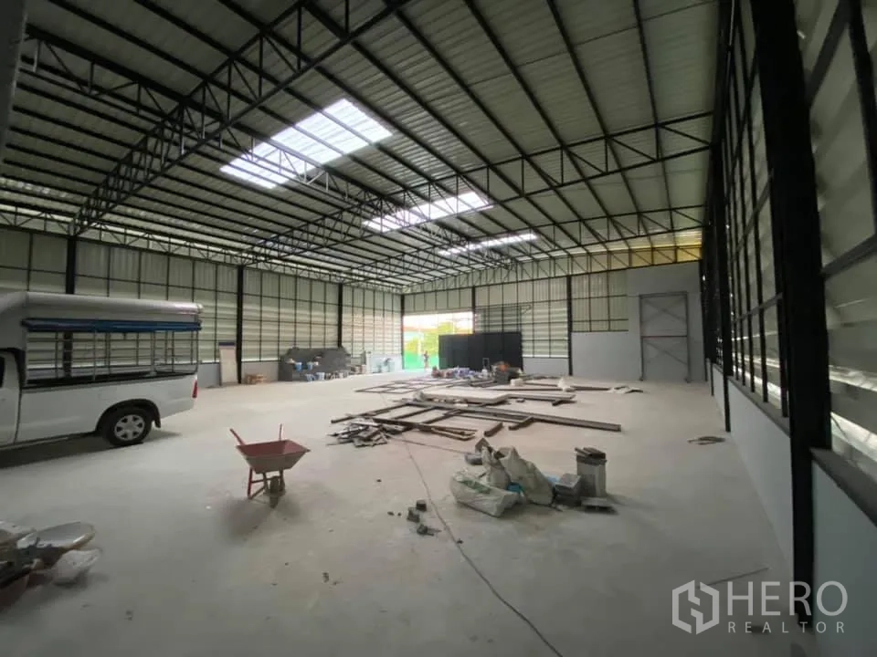 货栈 出租在Saphan Sung, Bangkok - 仓库内部空间宽敞，高钢结构屋架与天窗，混凝土地面，可见车辆与材料。