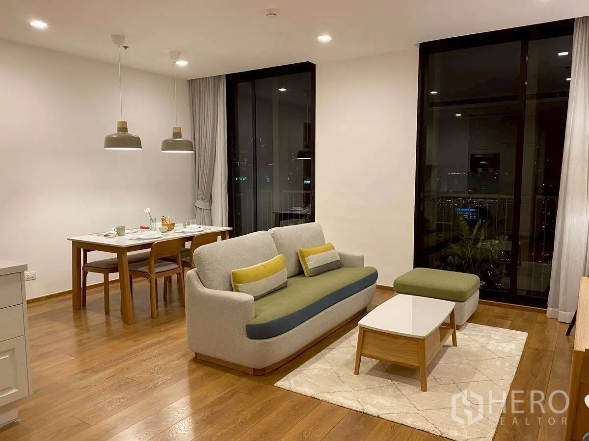 Condominium for rent in Watthana, Bangkok - Spacious living room at night with dining table and balcony doors.