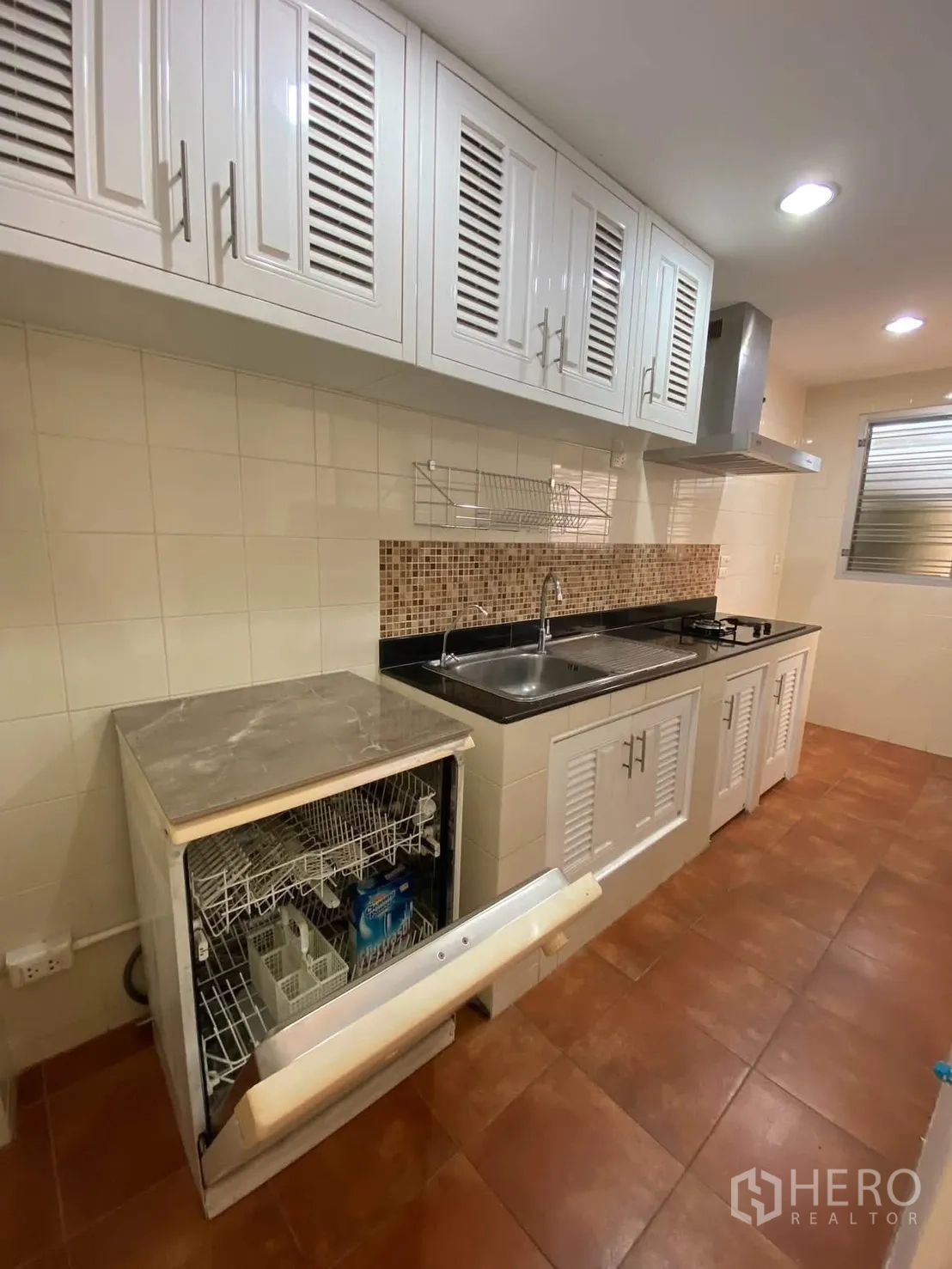 Detached House for rent in Mueang Samut Prakan, Samut Prakan - Fitted kitchen with white cabinets, cooktop, hood, and open dishwasher.