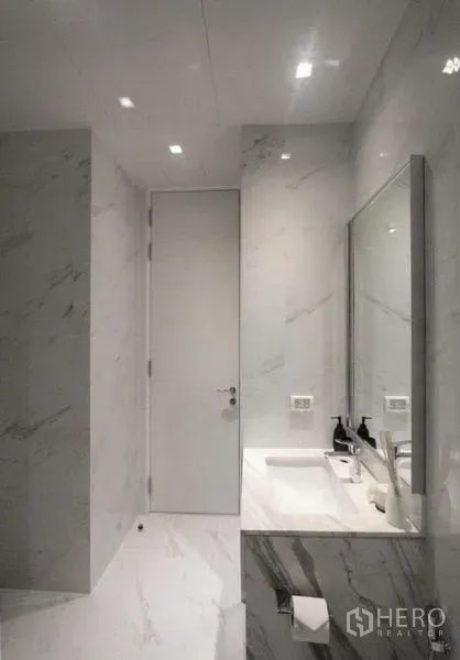 Condominium for rent in Bangkok - Modern bathroom finished in white marble with wide vanity, sink and framed mirror.