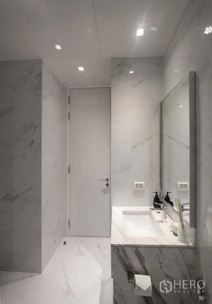 Condominium for rent in Bangkok - Modern bathroom finished in white marble with wide vanity, sink and framed mirror.