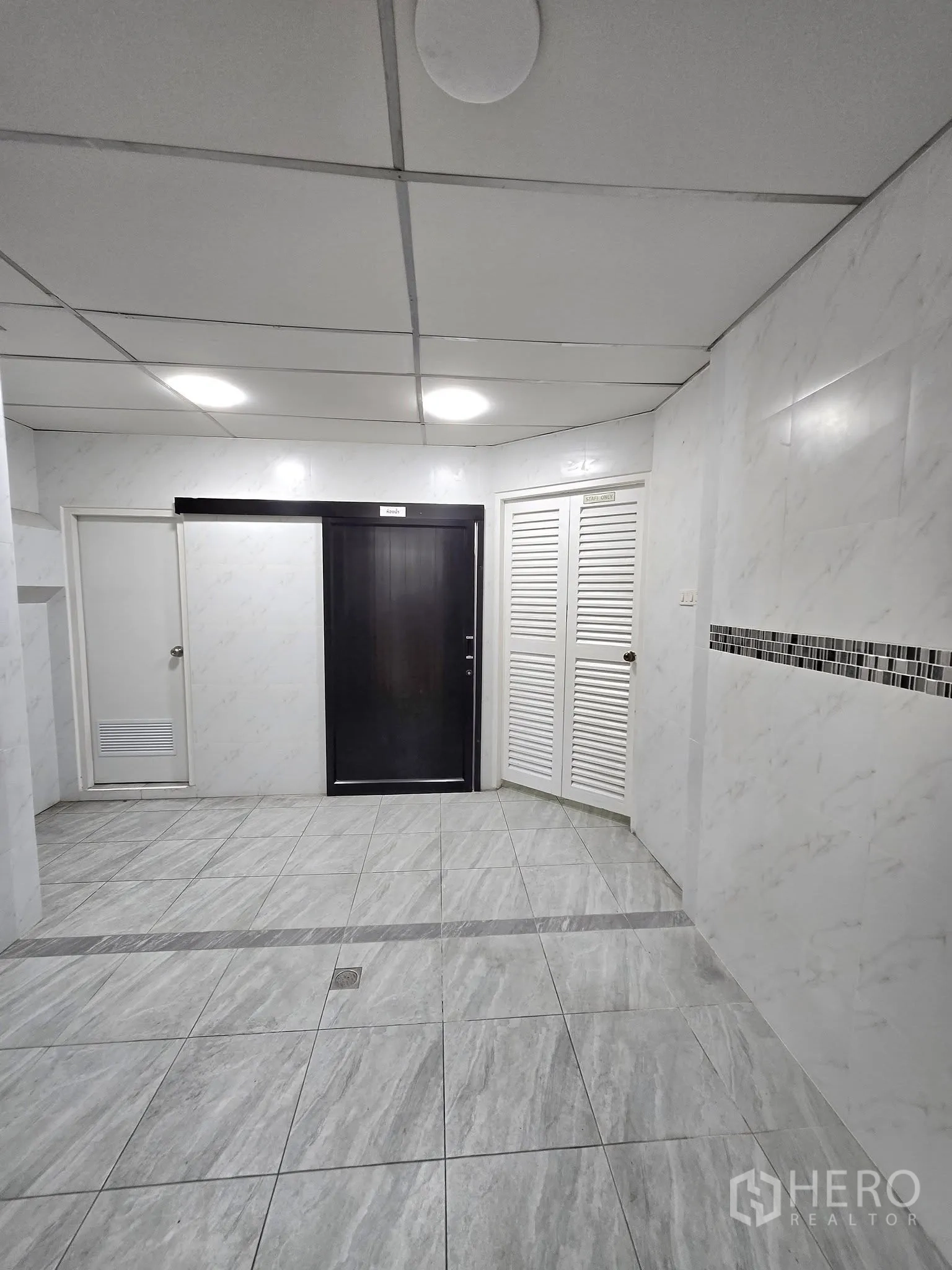 Office Space for rent in Khlong Toei, Bangkok - Bright tiled entry area with ceiling lights, a dark sliding door, and white louvered storage doors.